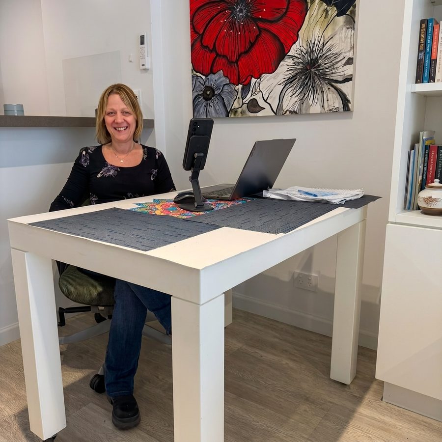 Lic. Laura Rabinovich sentada en su escritorio del consultorio, sonriendo junto a su notebook y su cuaderno